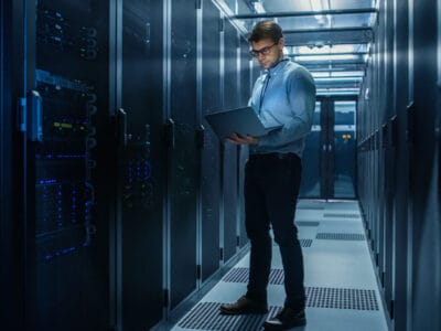 IT professional looks at his computer surrounded by banks of data storage.